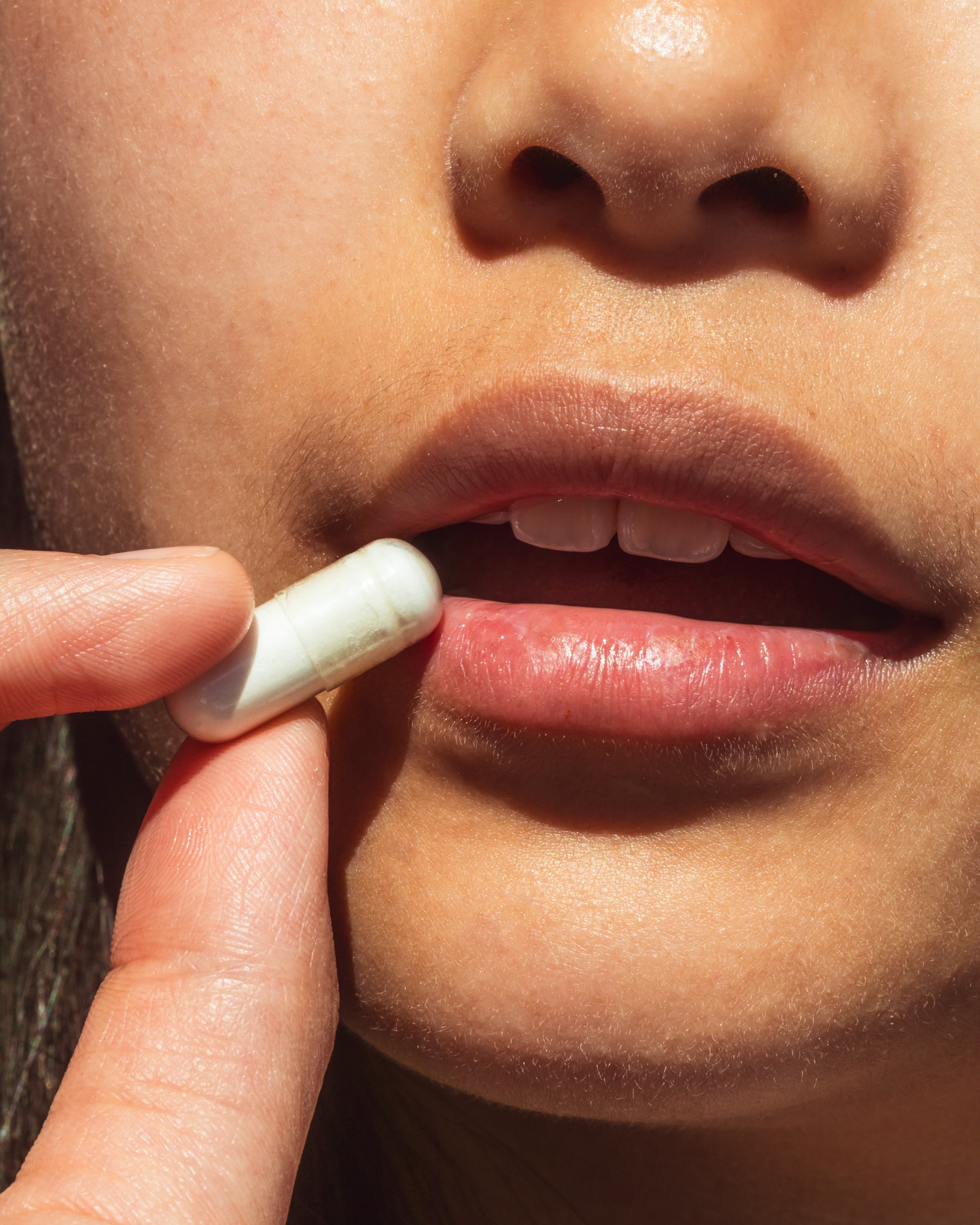 Nahaufnahme einer Frau, die eine weiße Kapsel zwischen den Fingern hält und gerade einnimmt – Symbol für BTONIC Bio-Precision Nahrungsergänzung und moderne Gesundheitsroutine.